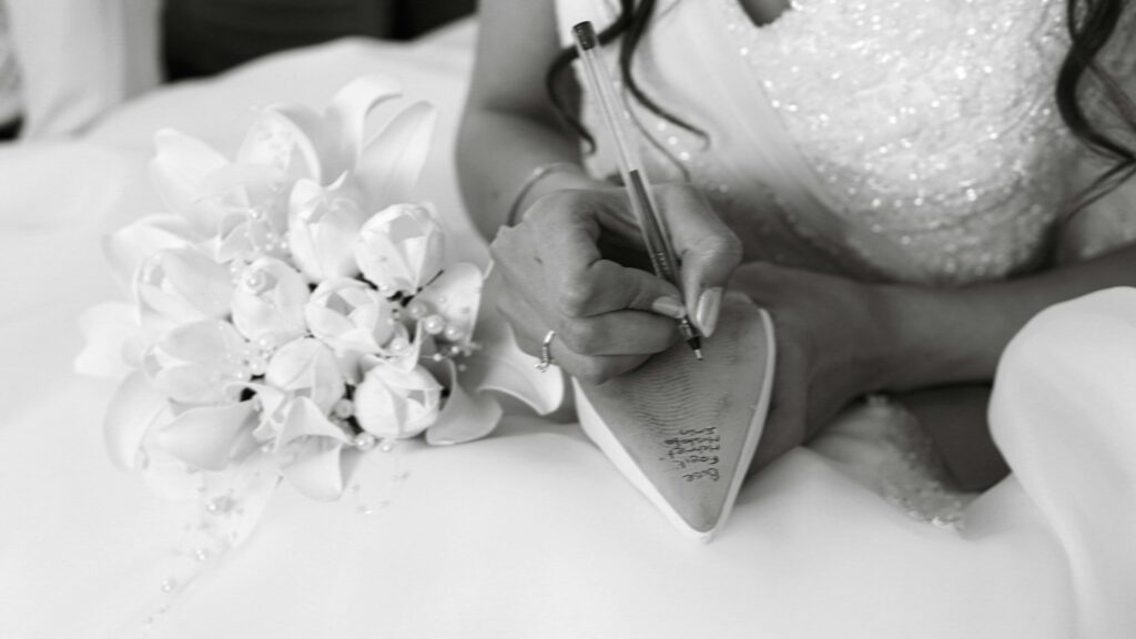 Bride inscribes names inside shoe at wedding, holding bouquet.