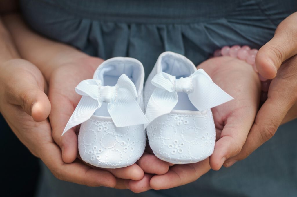 Close-up photo of hands holding white baby shoes with delicate bows, showcasing love and anticipation.